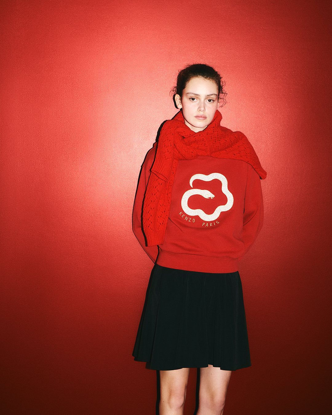 Model wearing a red sweatshirt and dark skirt against a vibrant red backdrop for Kenzo Lunar New Year campaign
