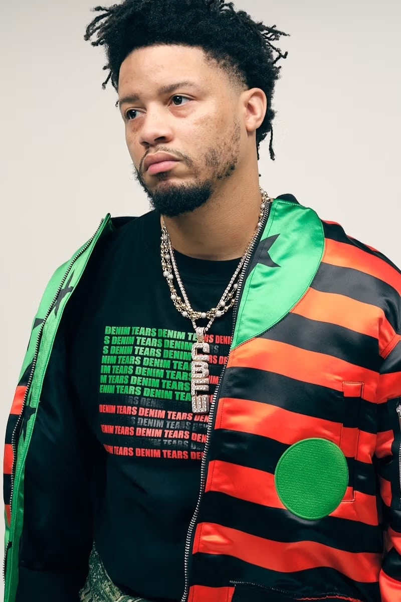 Model Veeze wearing a striped red, black, and green satin bomber jacket over a black graphic t-shirt against a white background