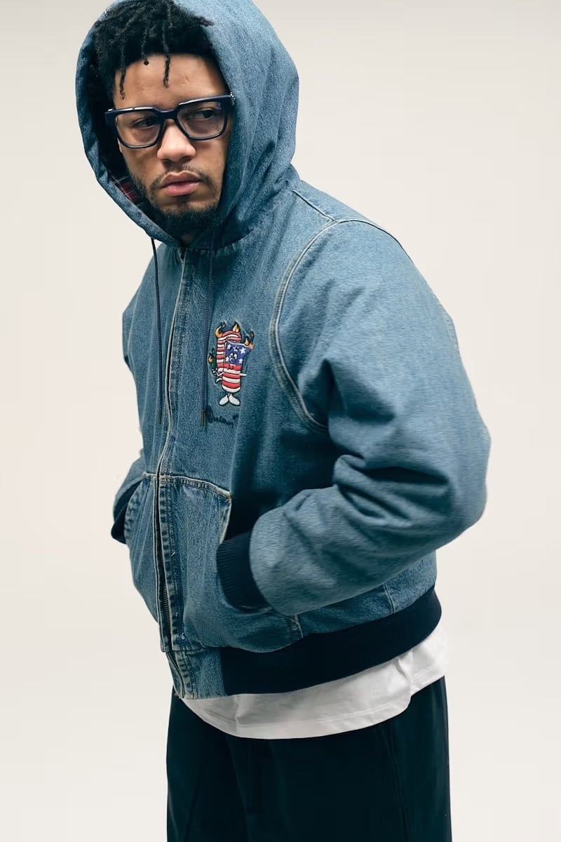 Man wearing a blue denim hoodie and black framed glasses against a seamless white background