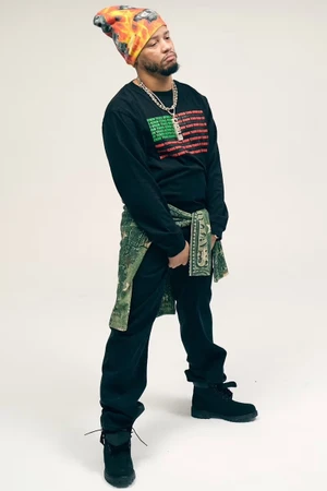 Model Veeze wearing a graphic long-sleeve shirt, beanie, and layered chains against a plain white studio backdrop.