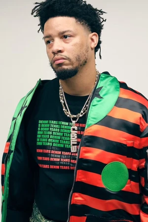 Model Veeze wearing a striped red, black, and green satin bomber jacket over a black graphic t-shirt against a white background
