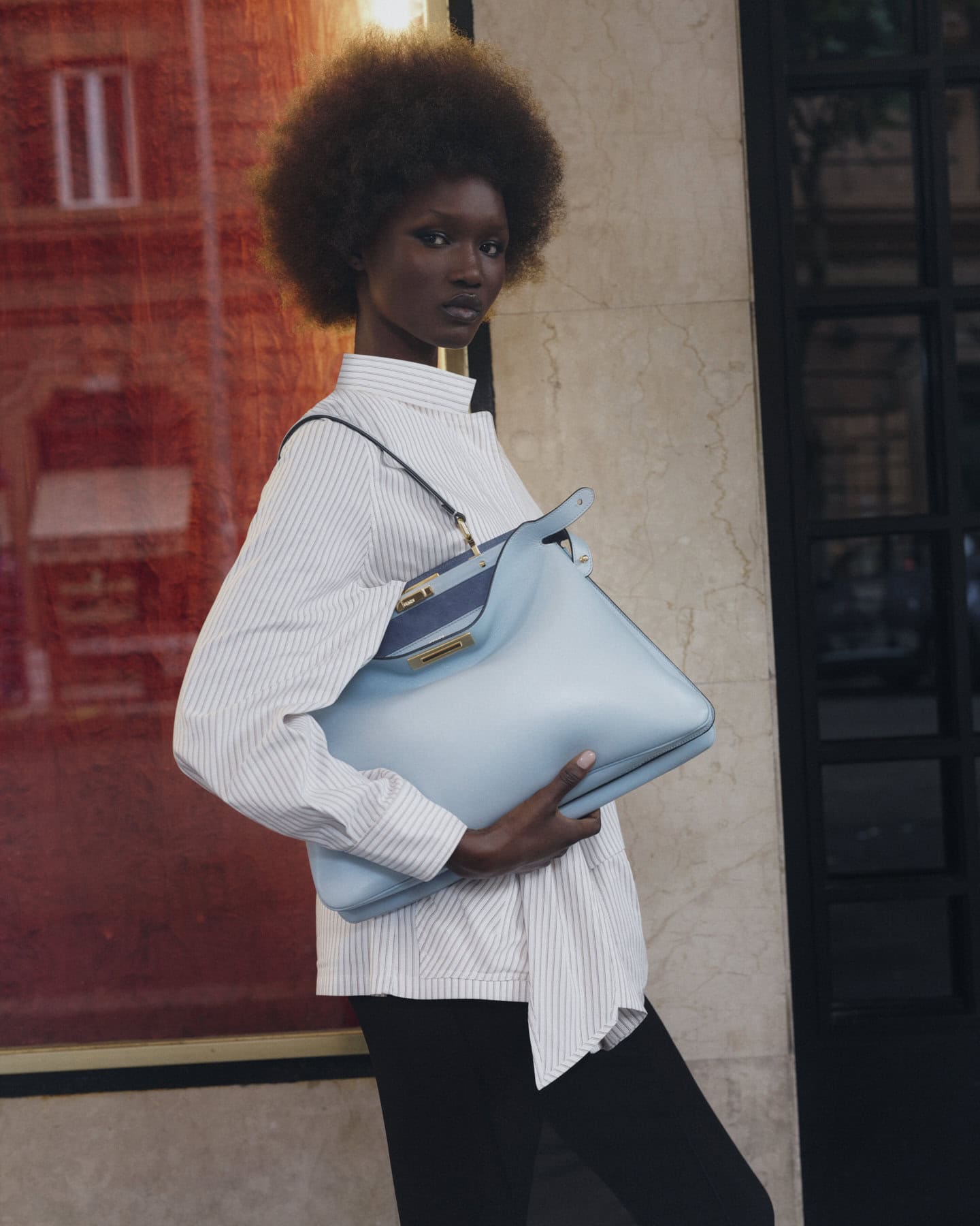 Black woman wearing a striped shirt holding a light blue Fendi handbag outdoors