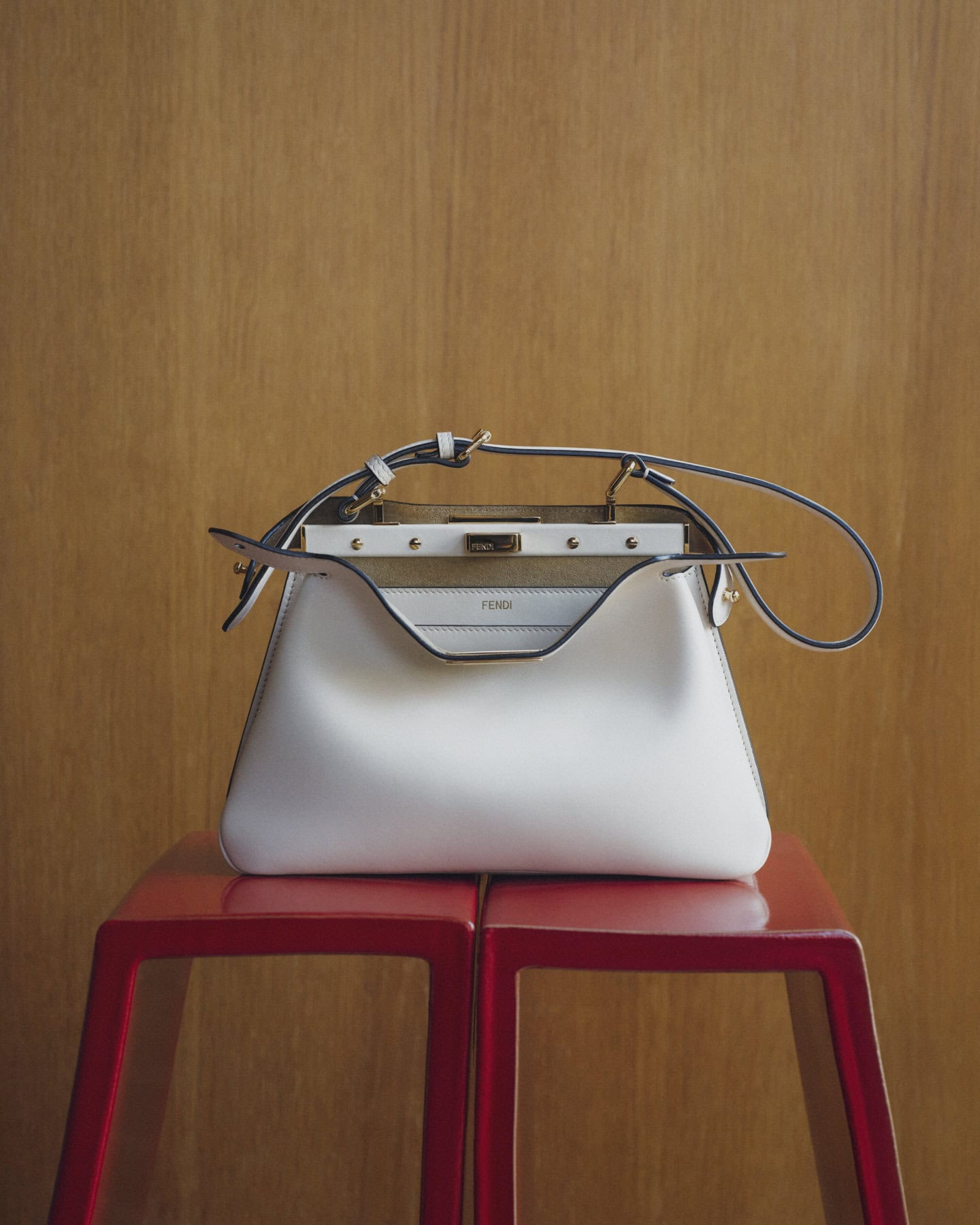 A white Fendi Peekaboo Soft Small handbag resting on two red stools against a wooden paneled wall.