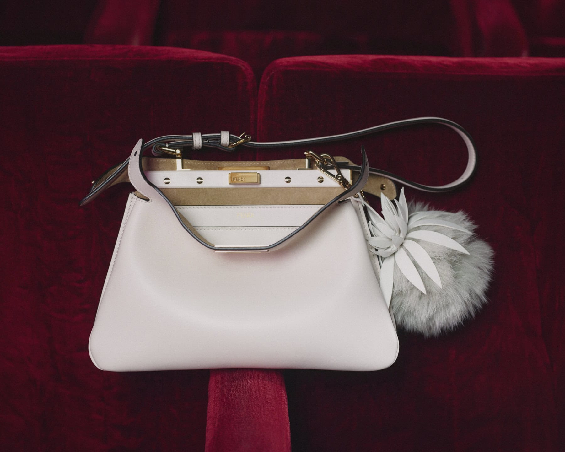Fendi Peekaboo Soft Small handbag resting on deep red velvet theater seats with a fluffy charm.