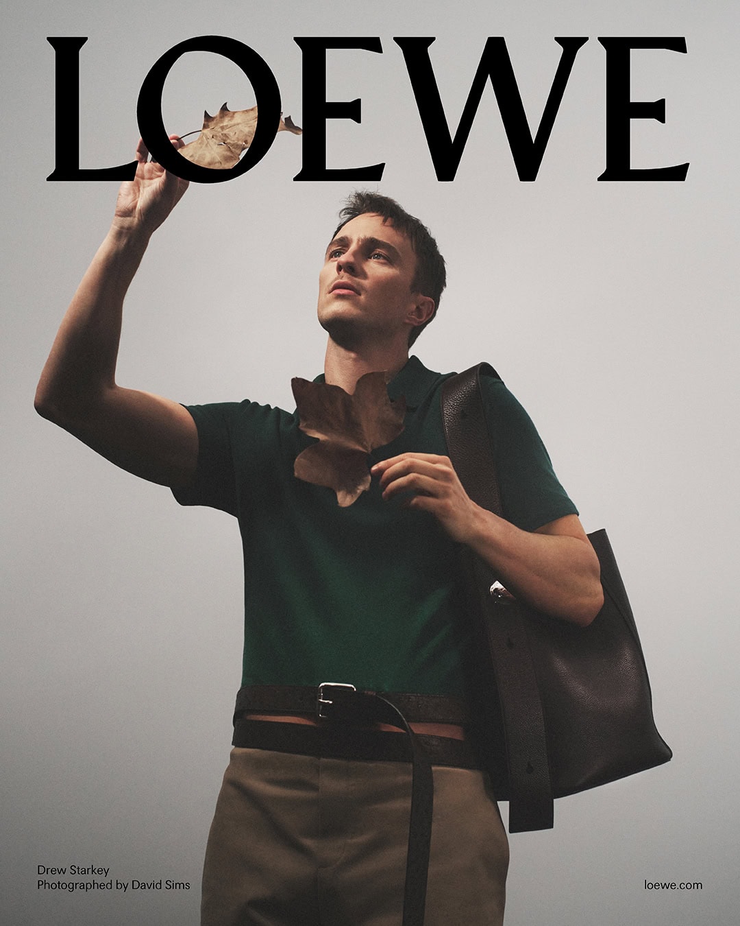 Drew Starkey in a green polo shirt holding dry leaves against an overcast sky for Loewe Spring 2025 campaign