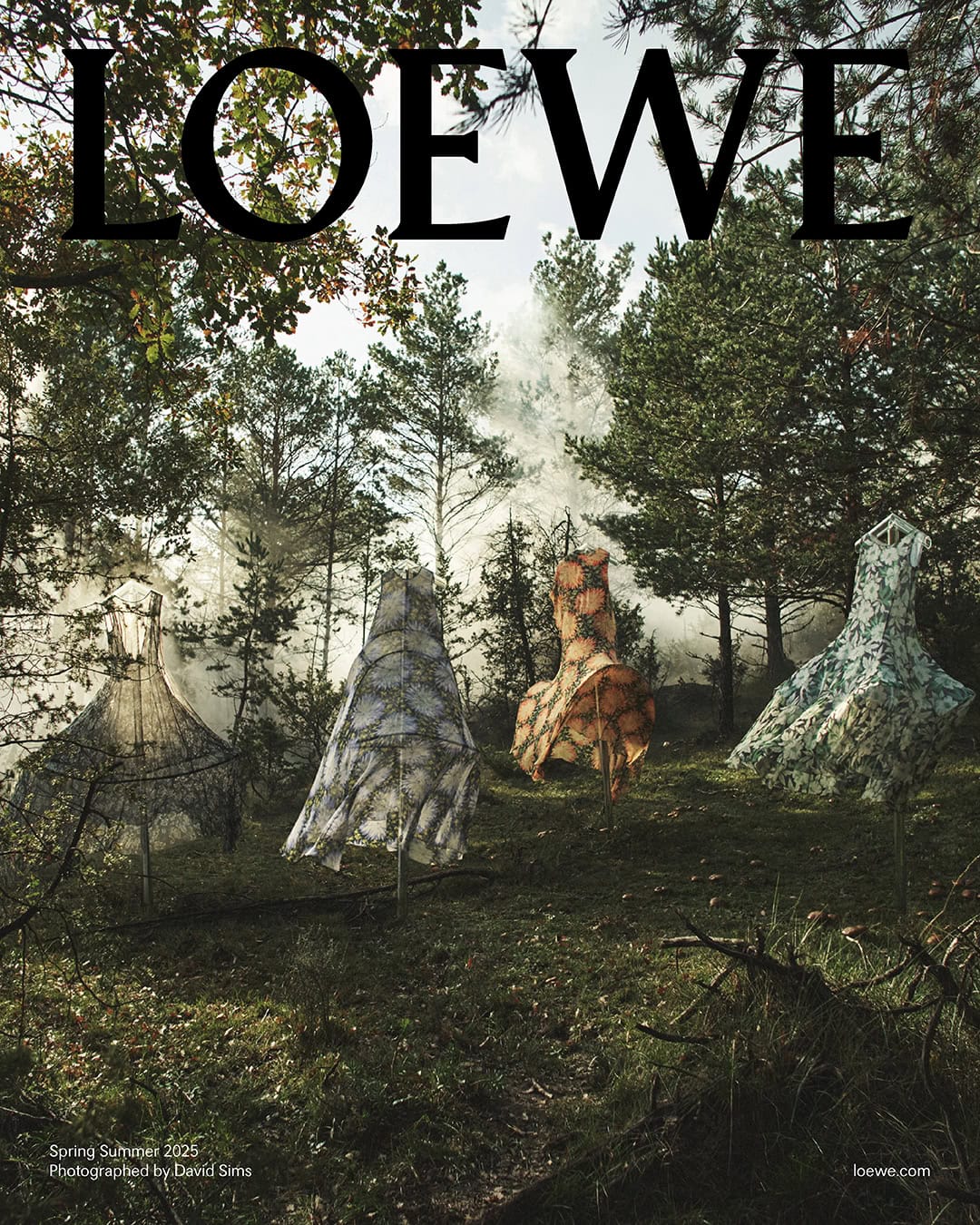 Four printed dresses displayed on stands in a misty woodland forest under soft daylight