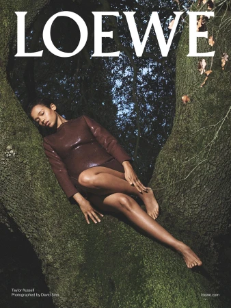 Taylor Russell reclining in the branches of a large tree wearing a dark brown long-sleeved dress for Loewe