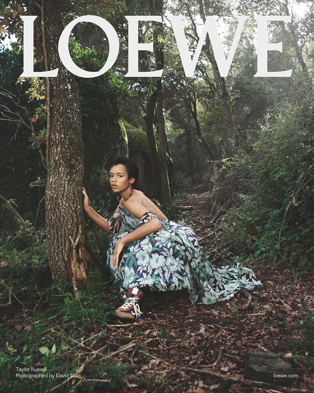 Taylor Russell crouching in a forest wearing a floral dress and hiking boots for Loewe Spring 2025 ad campaign.