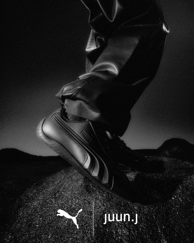Close-up shot of black Puma sneakers on a dark rocky surface for the Juun.J Speedcat ad campaign.
