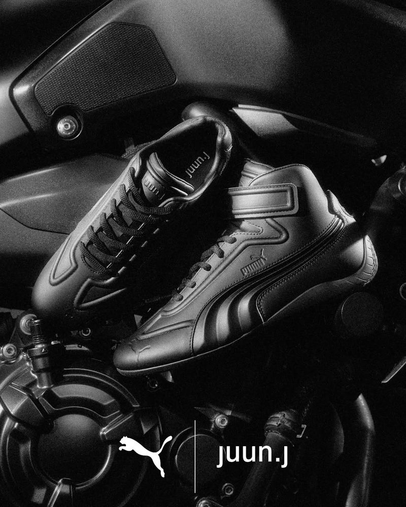 Black athletic sneakers resting on a dark motorcycle engine in a monochrome commercial photograph.