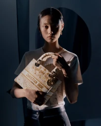 Model holding a patterned Dior handbag wearing a white t-shirt against a dark background