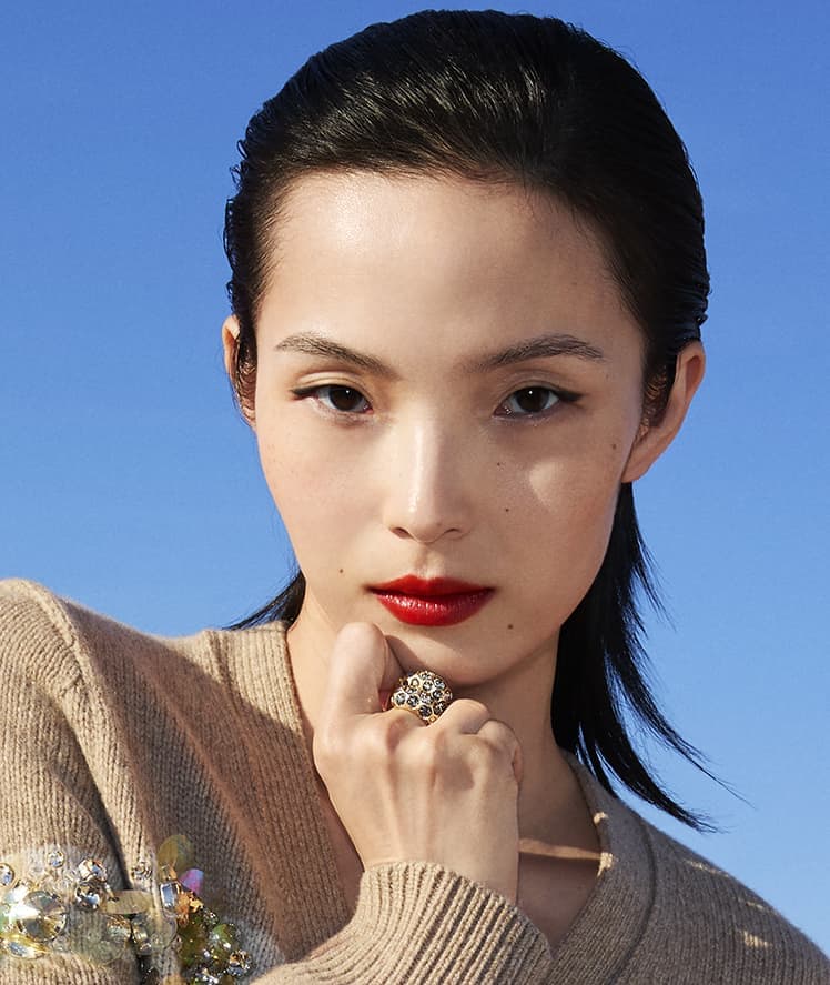 Model Xiao Wen Ju wearing a beige sweater with embellished details against a bright blue sky for Tory Burch
