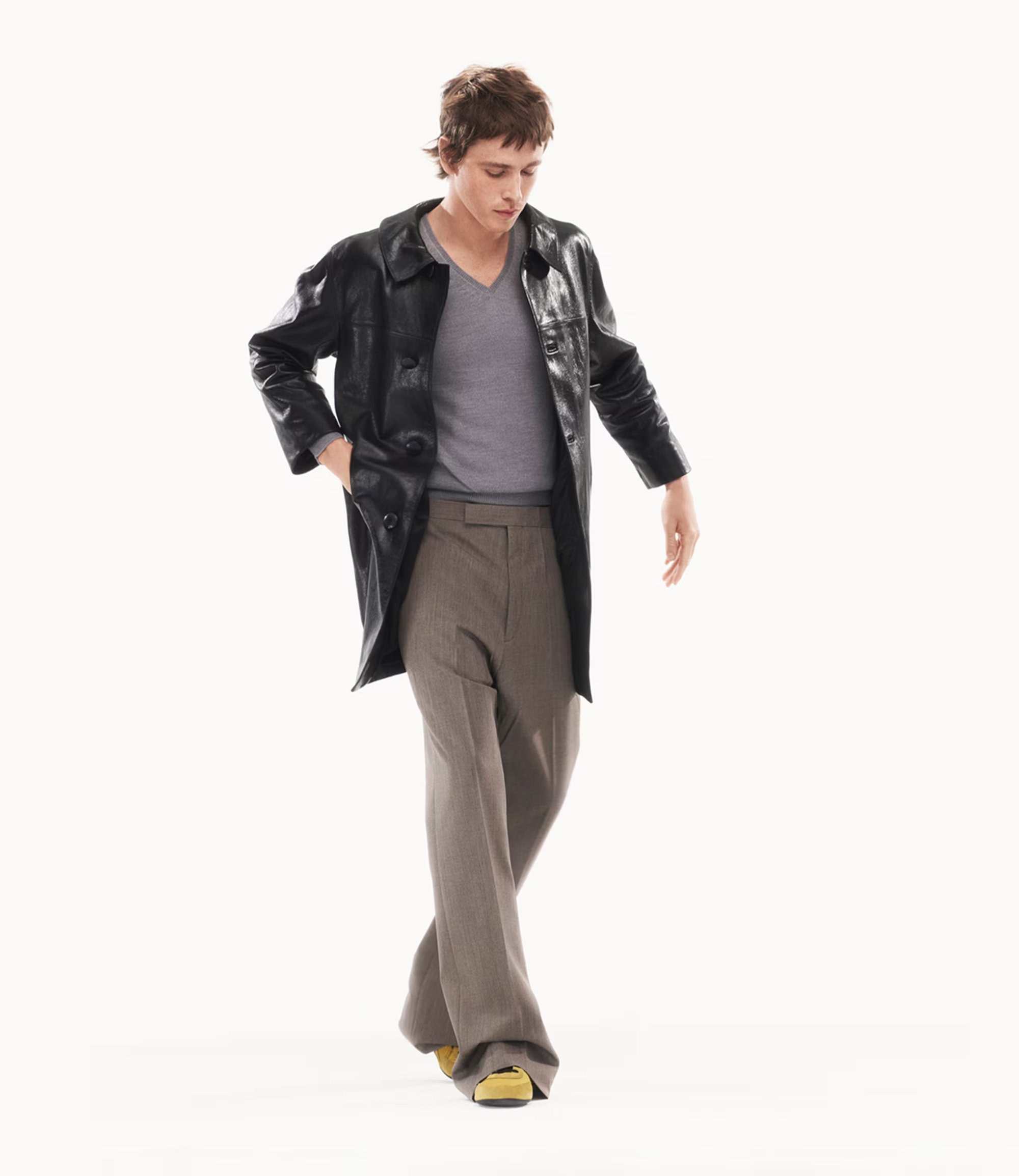 Harris Dickinson in a black leather coat and grey sweater posing against a white background for Prada.
