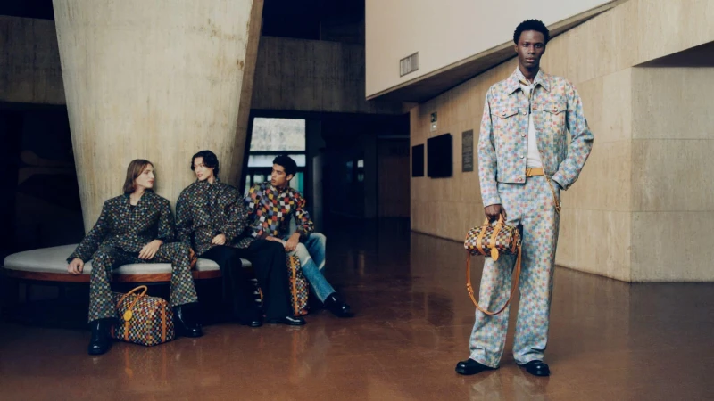 Four male models in checkered print outfits posing in a concrete interior with large pillars and polished floors for Louis Vuitton.