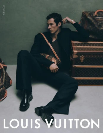 Man in black apparel seated on the floor leaning against luggage trunks with monogram print for Louis Vuitton campaign