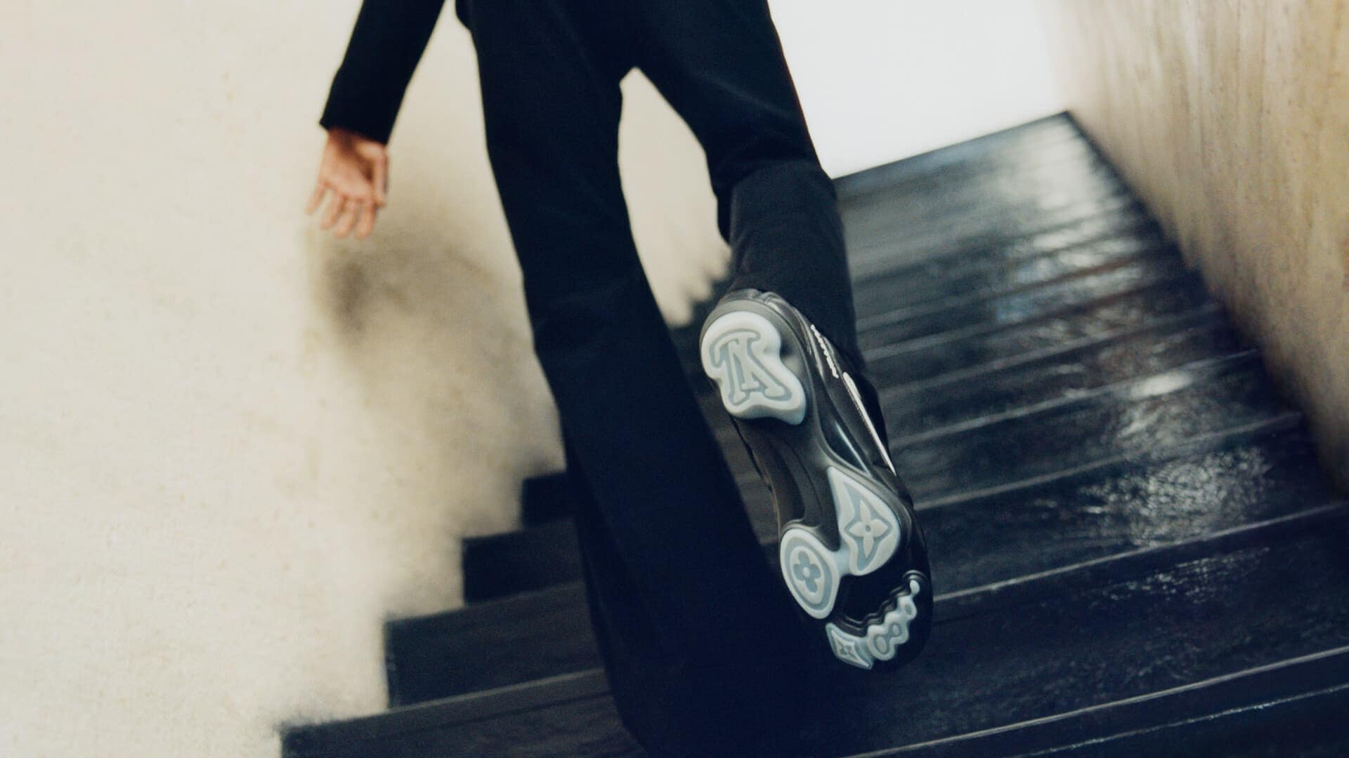 Low angle shot of a person walking up stairs wearing black trousers and designer sneakers with patterned soles