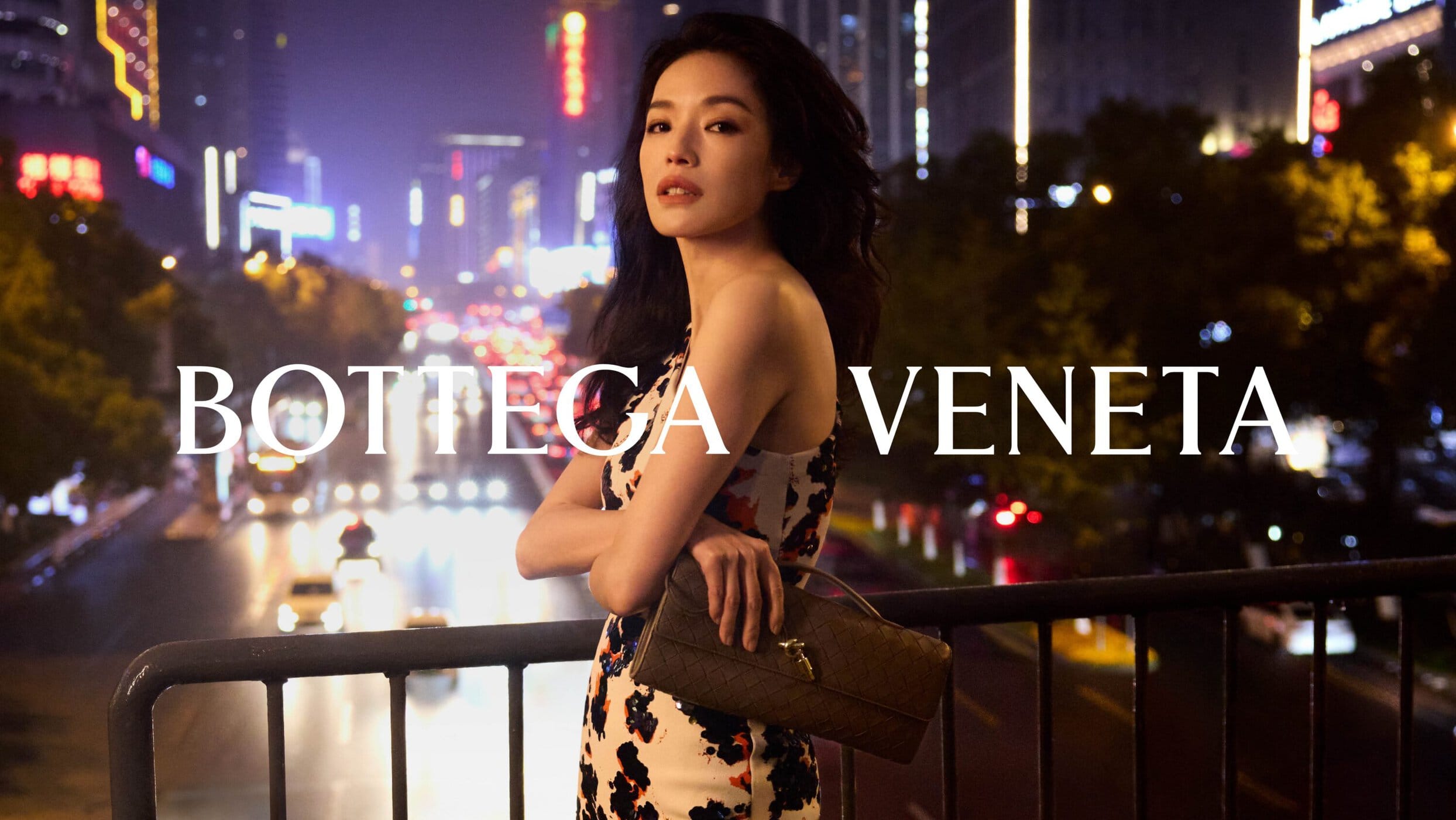 Actress Shu Qi holding a brown leather handbag on a city bridge at night for Bottega Veneta