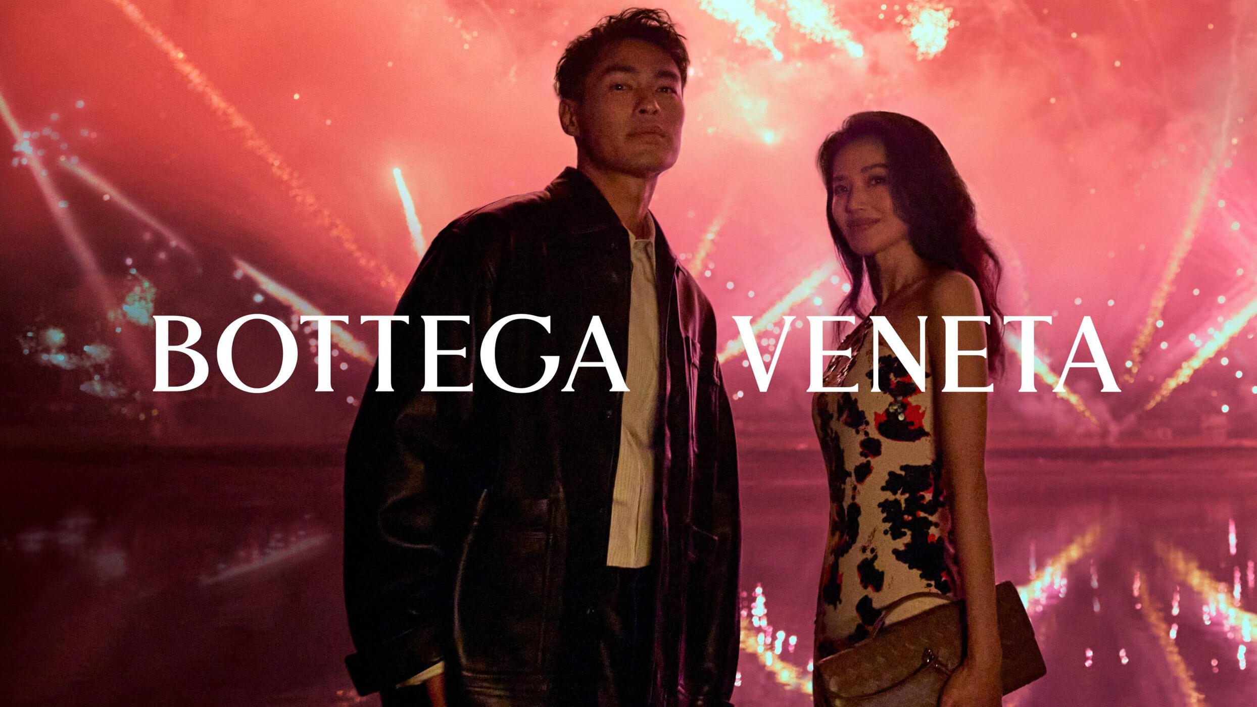 Man and woman standing against a vibrant pink fireworks display for Bottega Veneta Lunar New Year 2025 campaign.