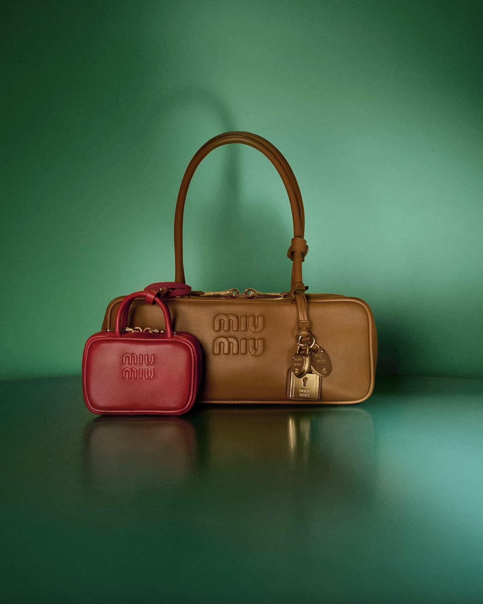 Tan leather shoulder bag and small red pouch with embossed logo against a green gradient background.