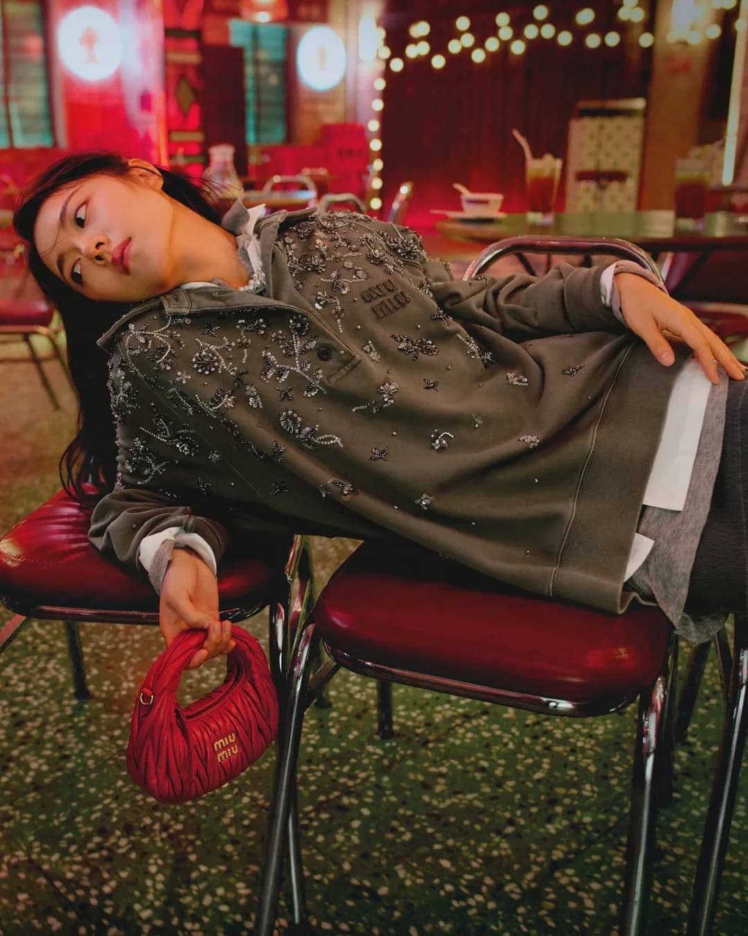 Young woman leaning back on red chairs holding a pink handbag for Miu Miu Lunar New Year campaign