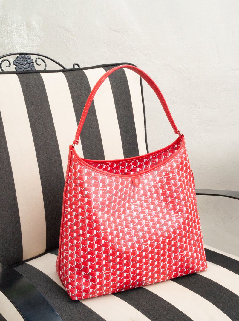 Red and white handbag with patterned design sitting on a striped upholstered chair. Interior shot with neutral wall background.