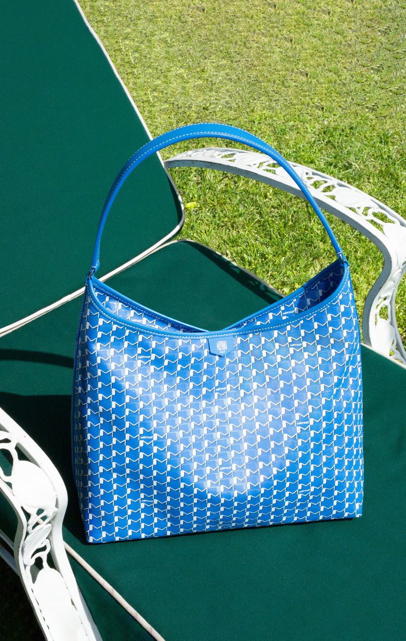 Blue and white patterned handbag with a single strap sits on a green cushioned chair outdoors in bright sunlight.