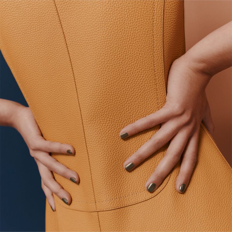Close-up of a person wearing a textured ochre leather garment with hands resting on hips against a color-blocked background.