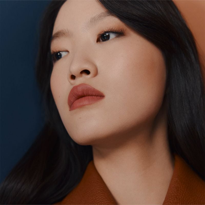 Close-up beauty portrait of a woman wearing warm lipstick against a divided blue and terracotta background.