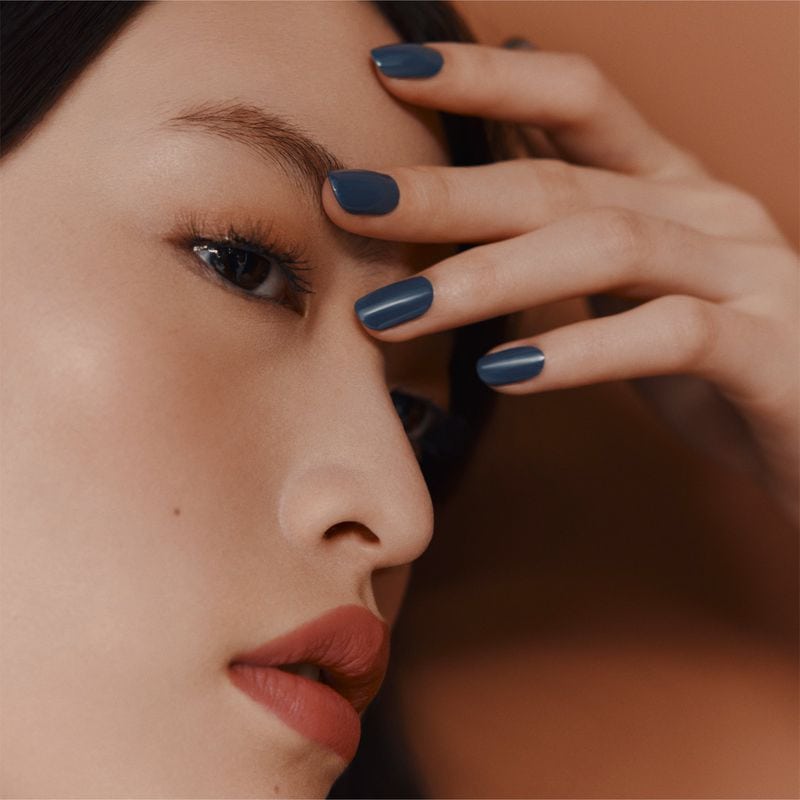 Close-up beauty portrait of a model showcasing dark blue glossy nail polish with a warm background.