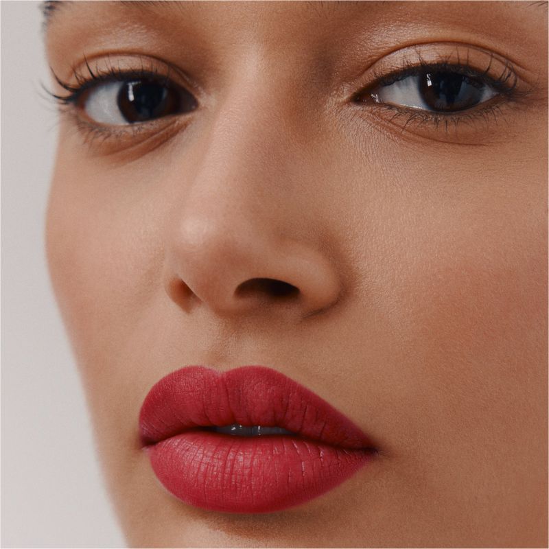 Close-up portrait of a model featuring vibrant red lipstick and clean skin against a neutral background for Hermes.