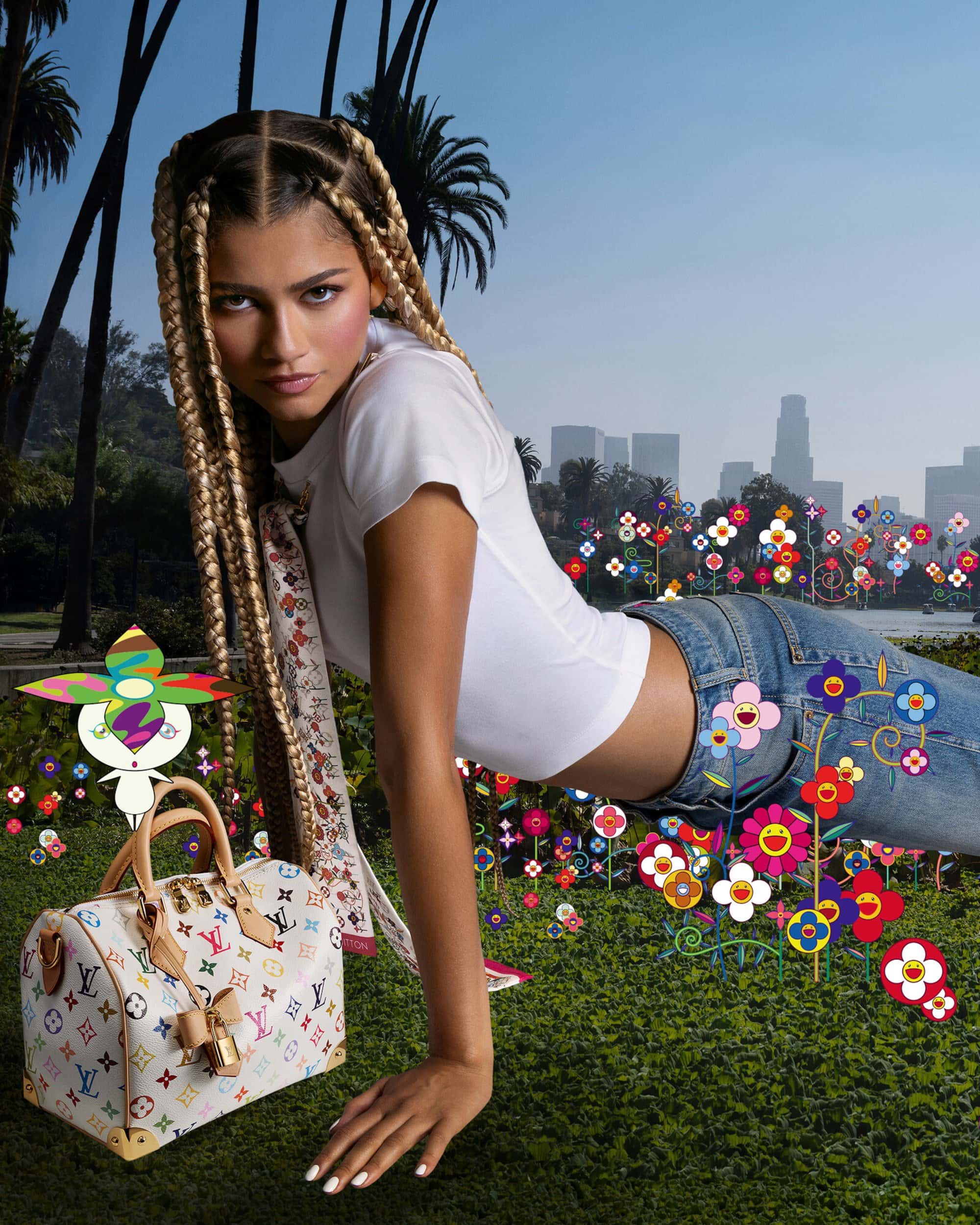Zendaya with long blonde braids wearing a white t-shirt and blue jeans, posing outdoors with a multicolored monogram handbag.