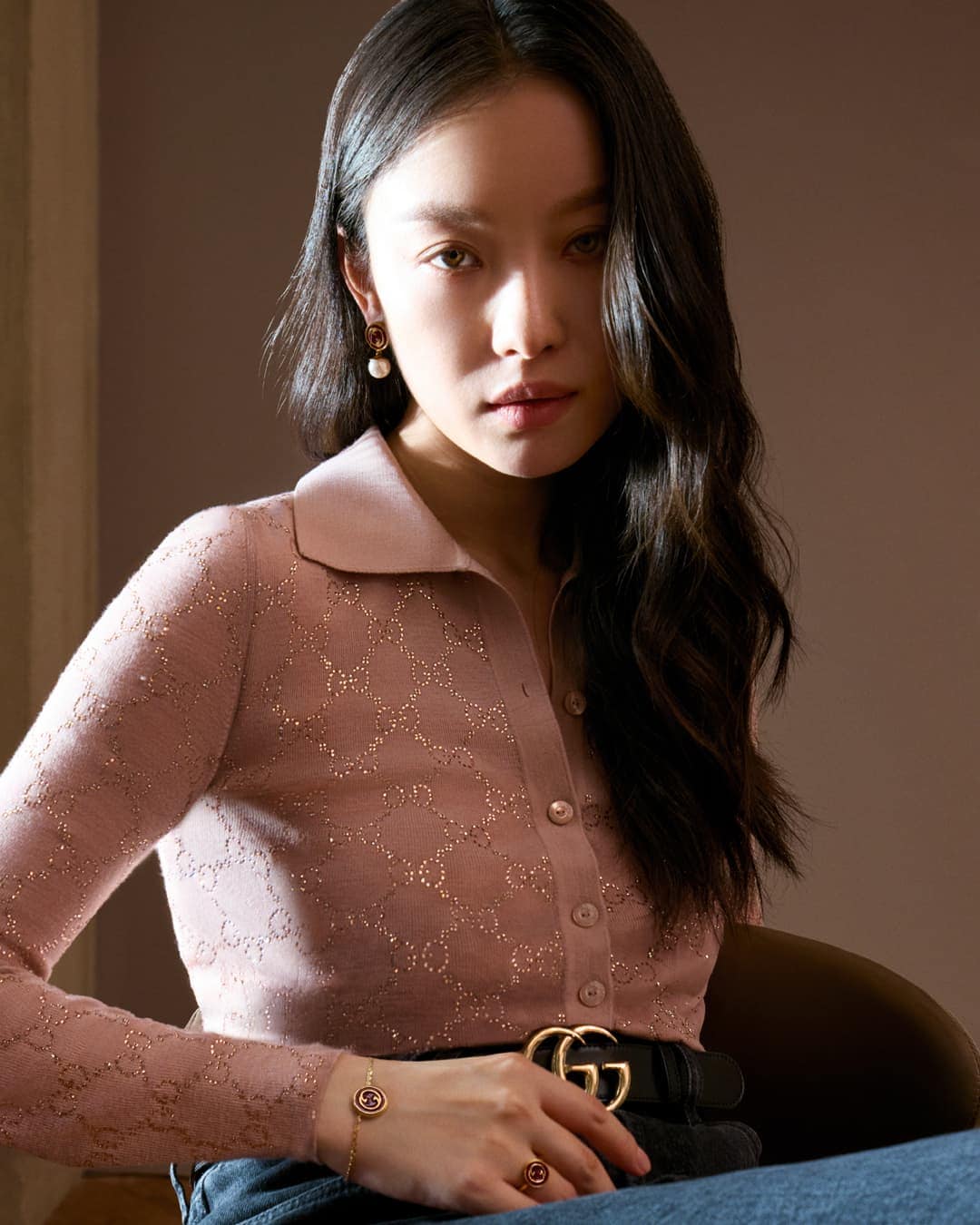 Portrait of an East Asian woman wearing a pink monogram polo shirt and pearl earrings for Gucci Lunar New Year campaign