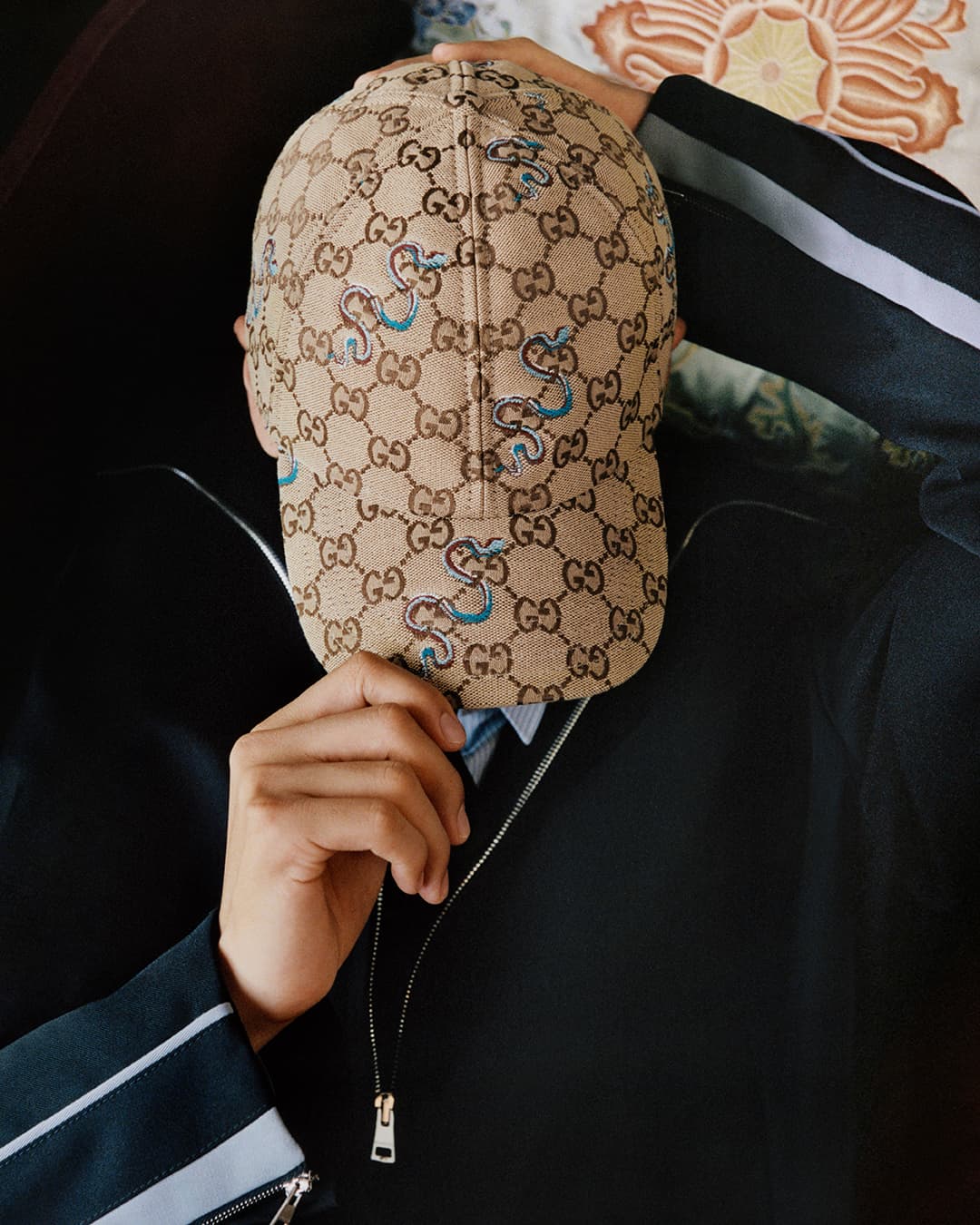 Person wearing a monogram baseball cap and black jacket with white stripes for Gucci Lunar New Year 2025 campaign.