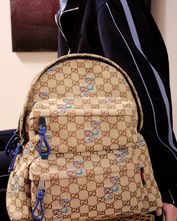 Gucci monogram backpack featuring embroidered blue snake motifs worn against a dark jacket