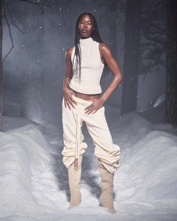 Model with long braided hair wearing cream sleeveless top and trousers in snowy forest