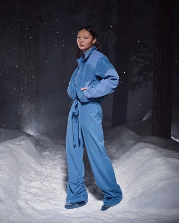 Model standing outdoors in a snowy forest wearing a blue fleece jacket and blue trousers during an ad campaign