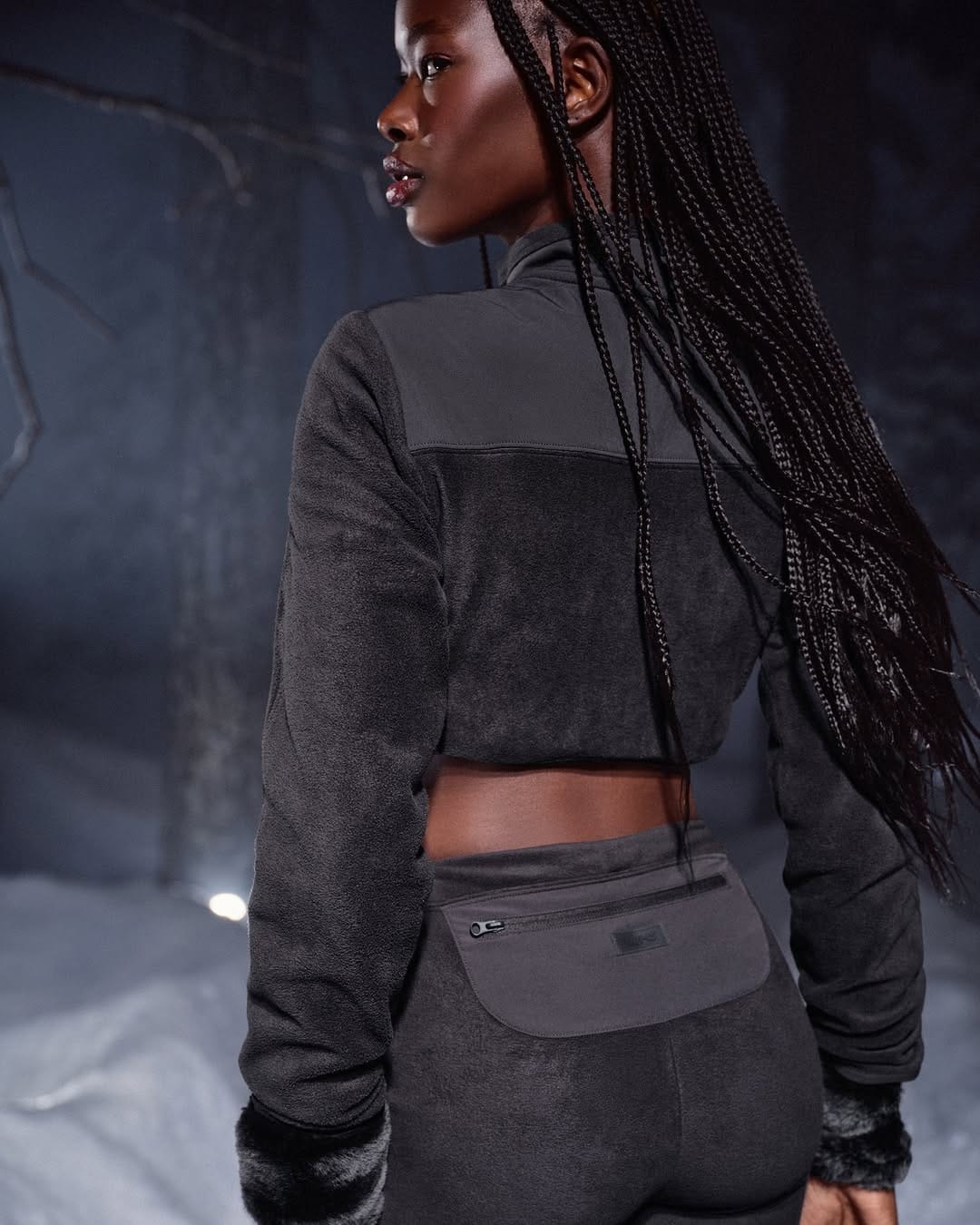 Model with long dark braids wearing a grey fleece zip jacket and matching pants outdoors in winter