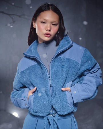 Model wearing a blue fleece jacket against an atmospheric snowy outdoor backdrop for SKIMS Cold Weather campaign.