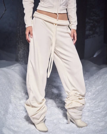 Model wearing cream colored sweatpants and matching zip jacket standing outdoors on snow in a winter setting.
