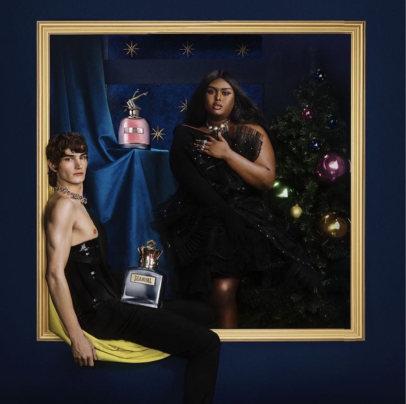 Jean Paul Gaultier fragrance campaign featuring two models inside a large gold-framed holiday set with perfume bottles.
