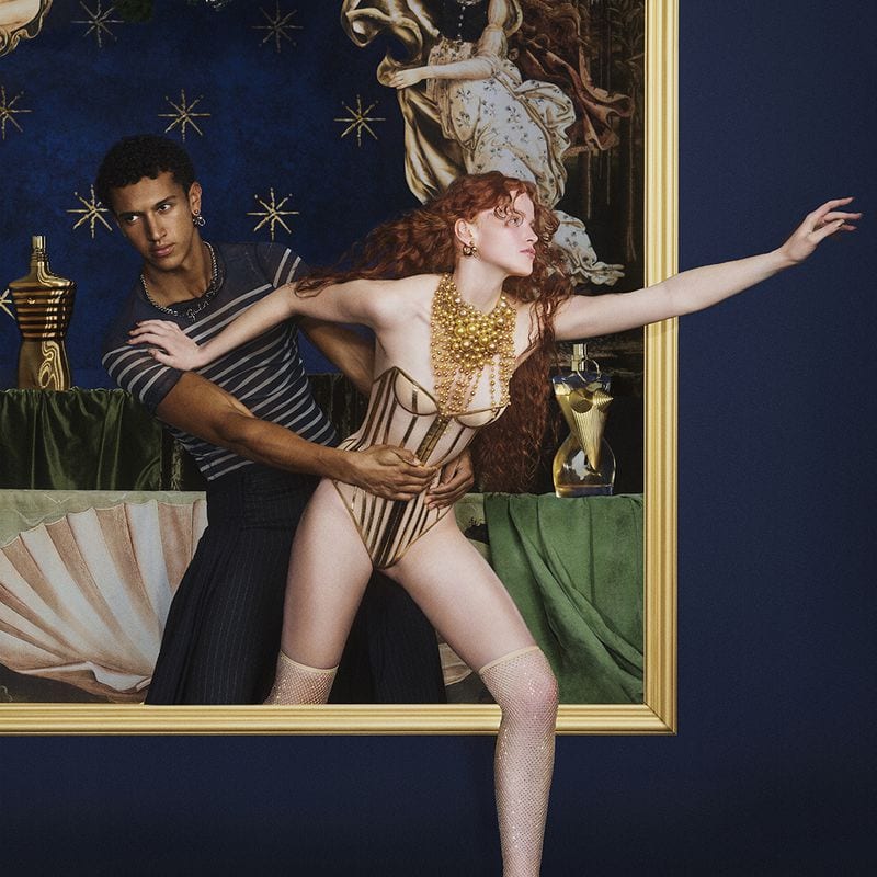 Models posing inside a gilded picture frame against a dark blue studio background for a Jean Paul Gaultier campaign.