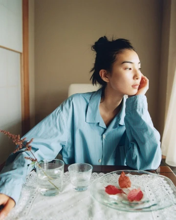 Model wearing a light blue button-down shirt seated at a table with glasses of water and red autumn leaves.