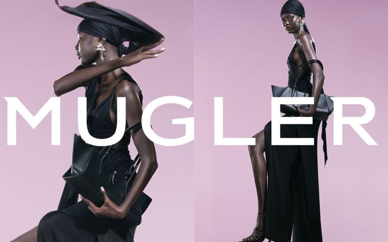 Model wearing a black dress, matching headwrap, and large earrings holding a structured handbag against a pink background