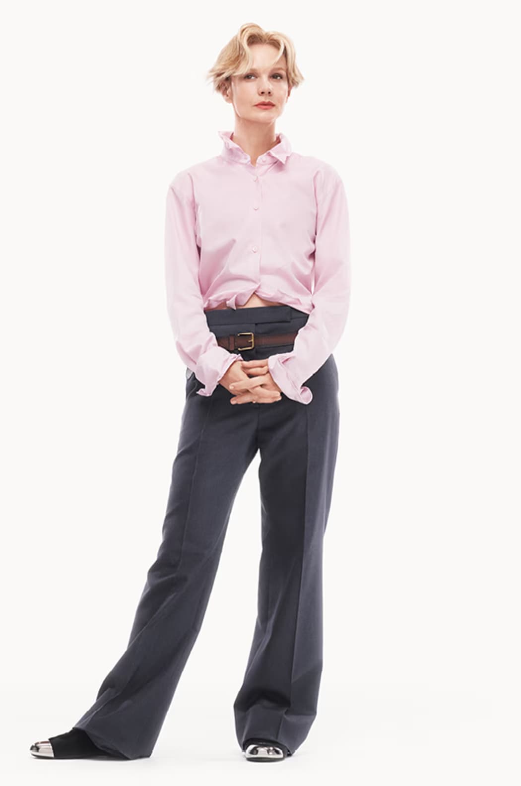 Carey Mulligan wearing a pink button-down shirt and grey trousers against a plain white background for Prada