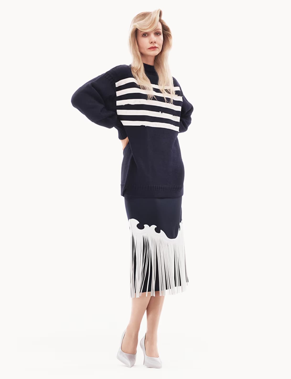 Carey Mulligan wearing a navy striped sweater and fringed skirt against a white studio background