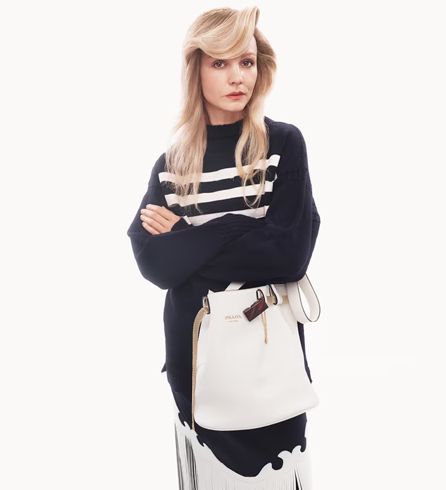 Carey Mulligan in a black sweater and patterned skirt holding a white Prada bucket bag against a white background
