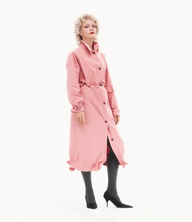 Carey Mulligan in a pink trench coat wearing dark tights and heels against a white seamless background for Prada
