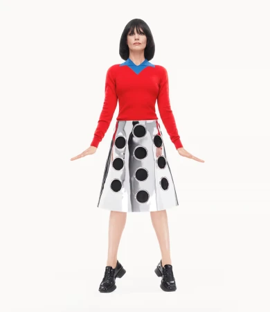 Carey Mulligan in a red sweater and metallic skirt standing against a bright white background for Prada Spring 2025 campaign.