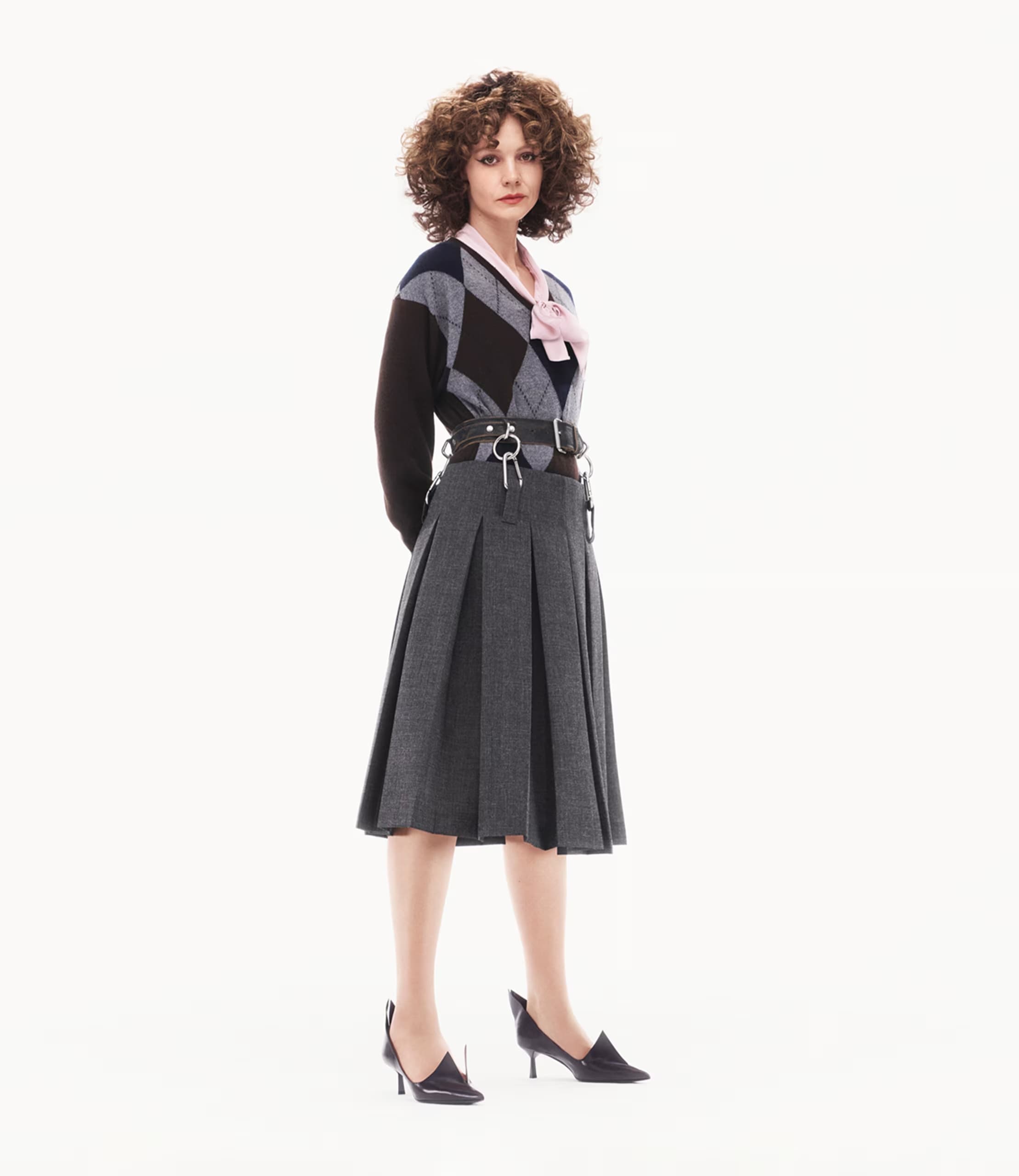 Carey Mulligan wearing argyle sweater and pleated skirt against a plain white background for Prada spring 2025 ad campaign.