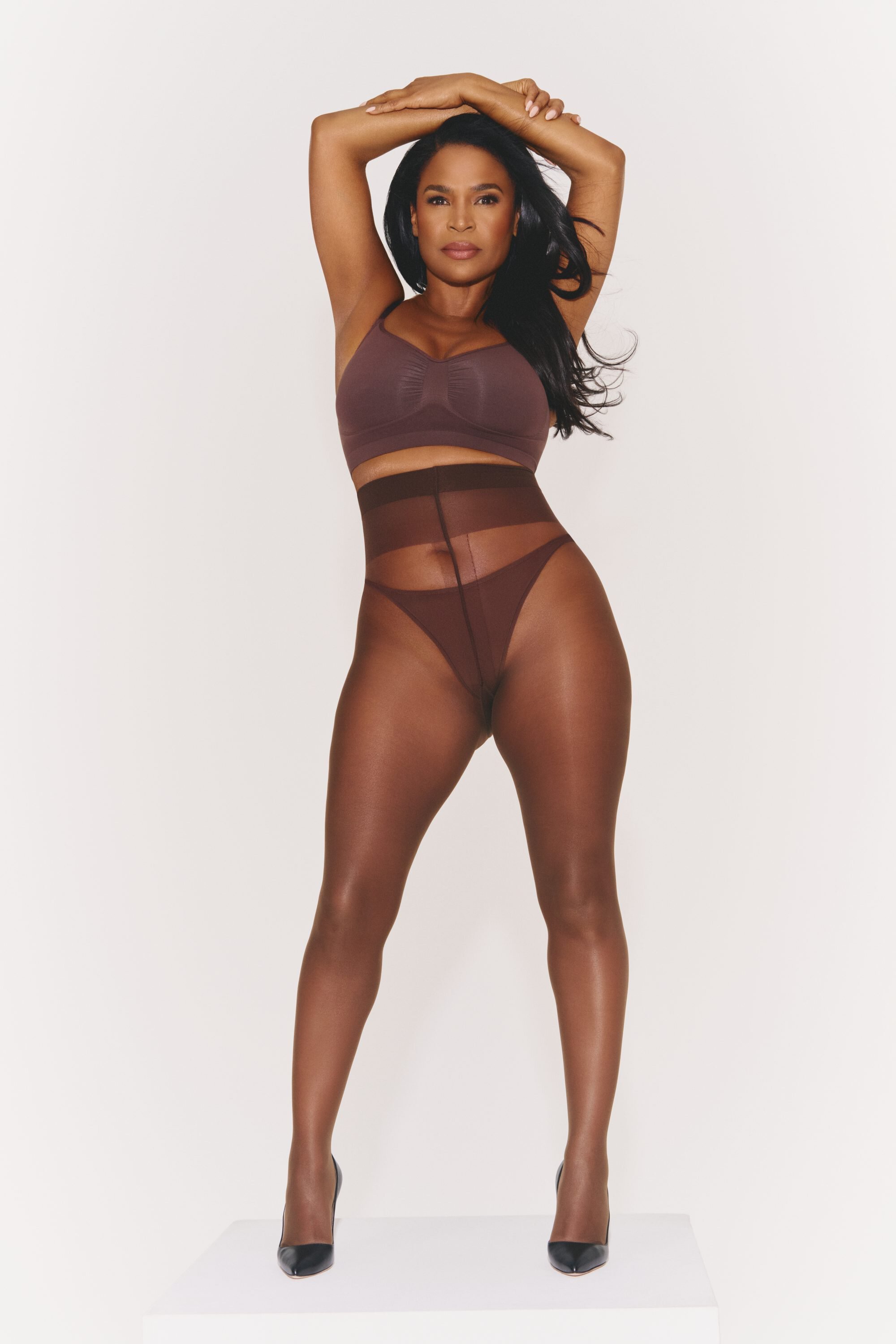 Nia Long posing in brown SKIMS shapewear and bralette against a seamless white studio background